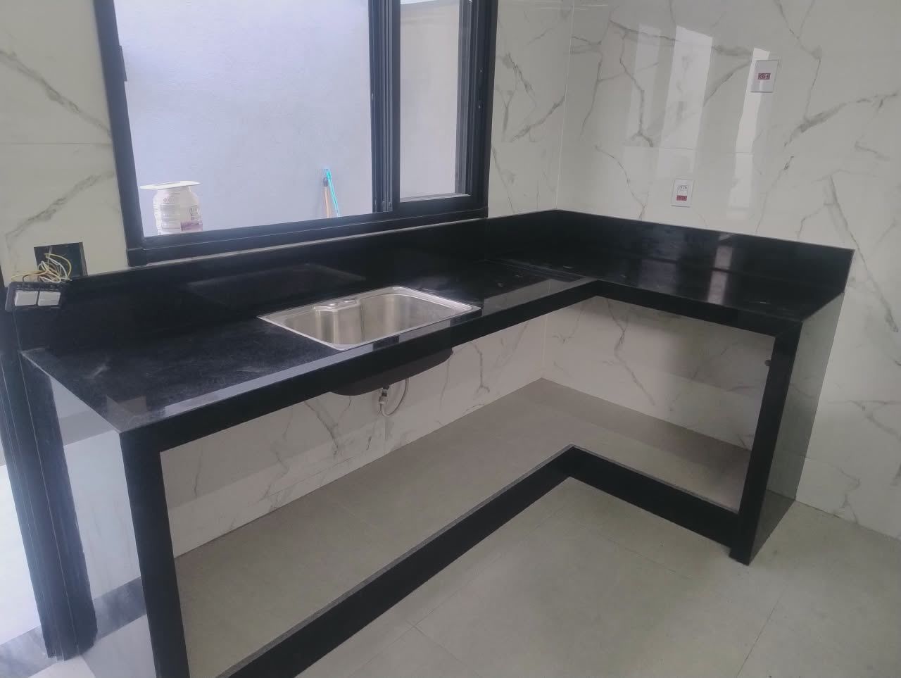 Bancada em L de granito preto com base e rodapé na mesma pedra