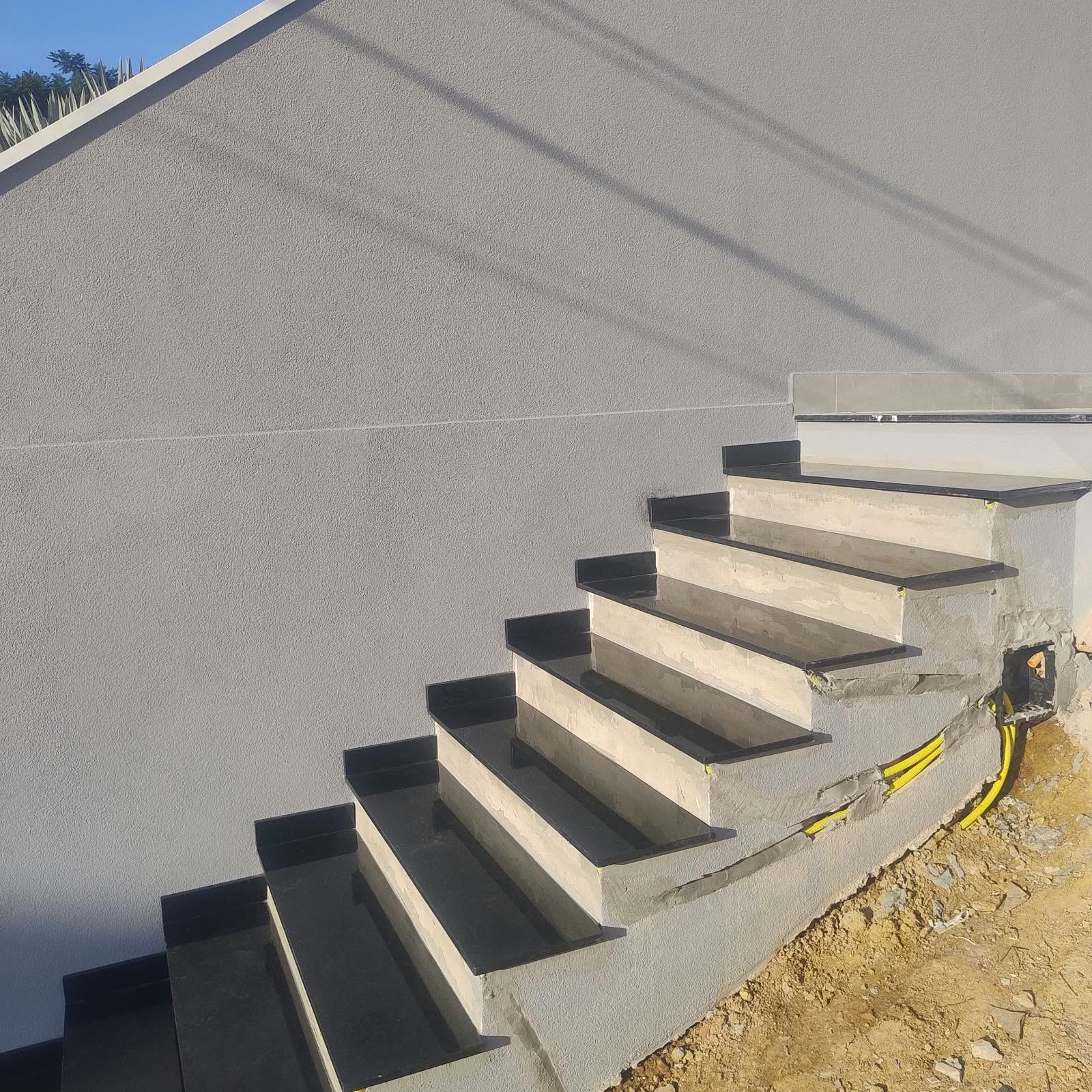Escada externa com degraus de granito preto junto a um muro cinza