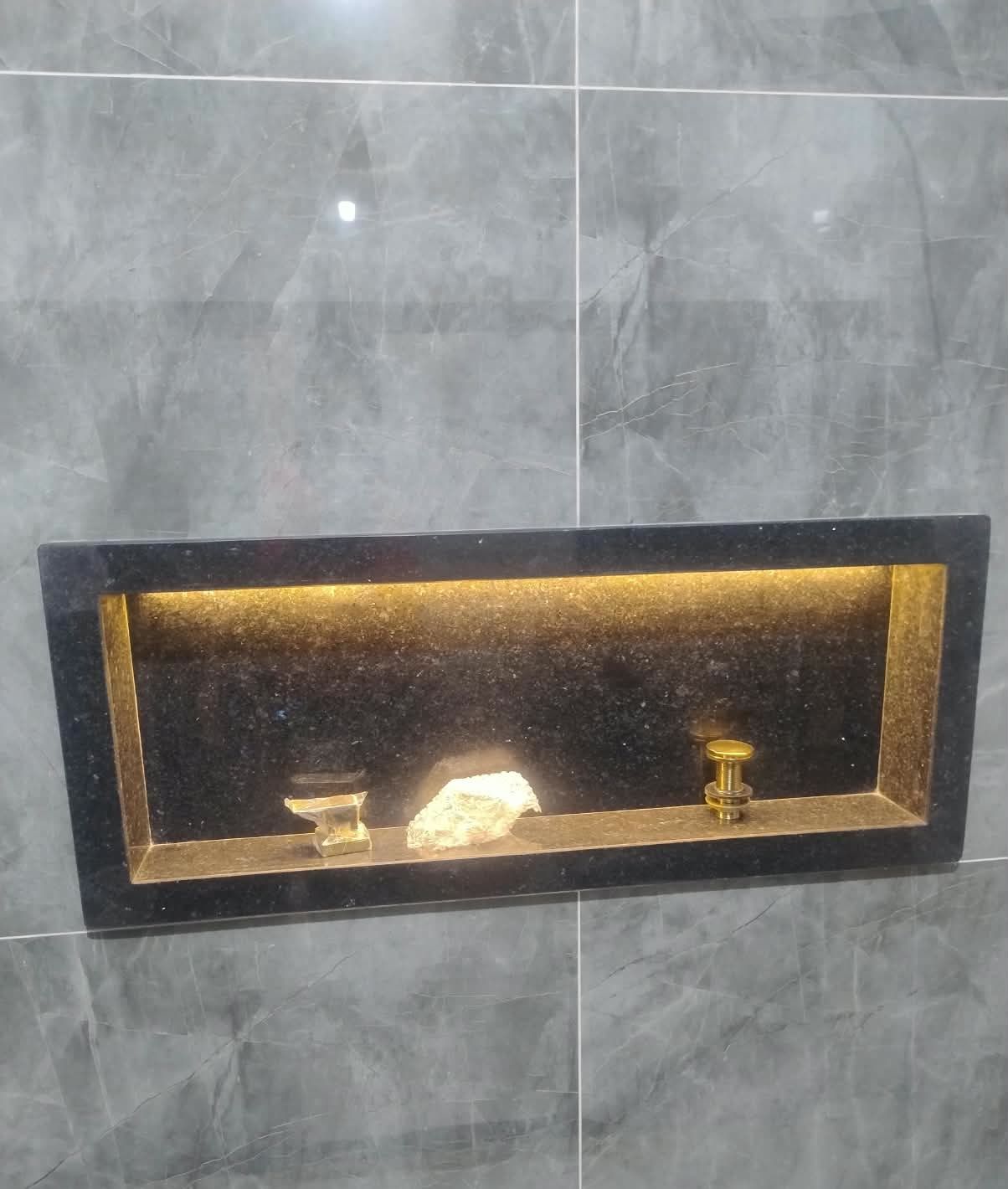 Nicho de box em granito escuro com fita de LED e metais dourados