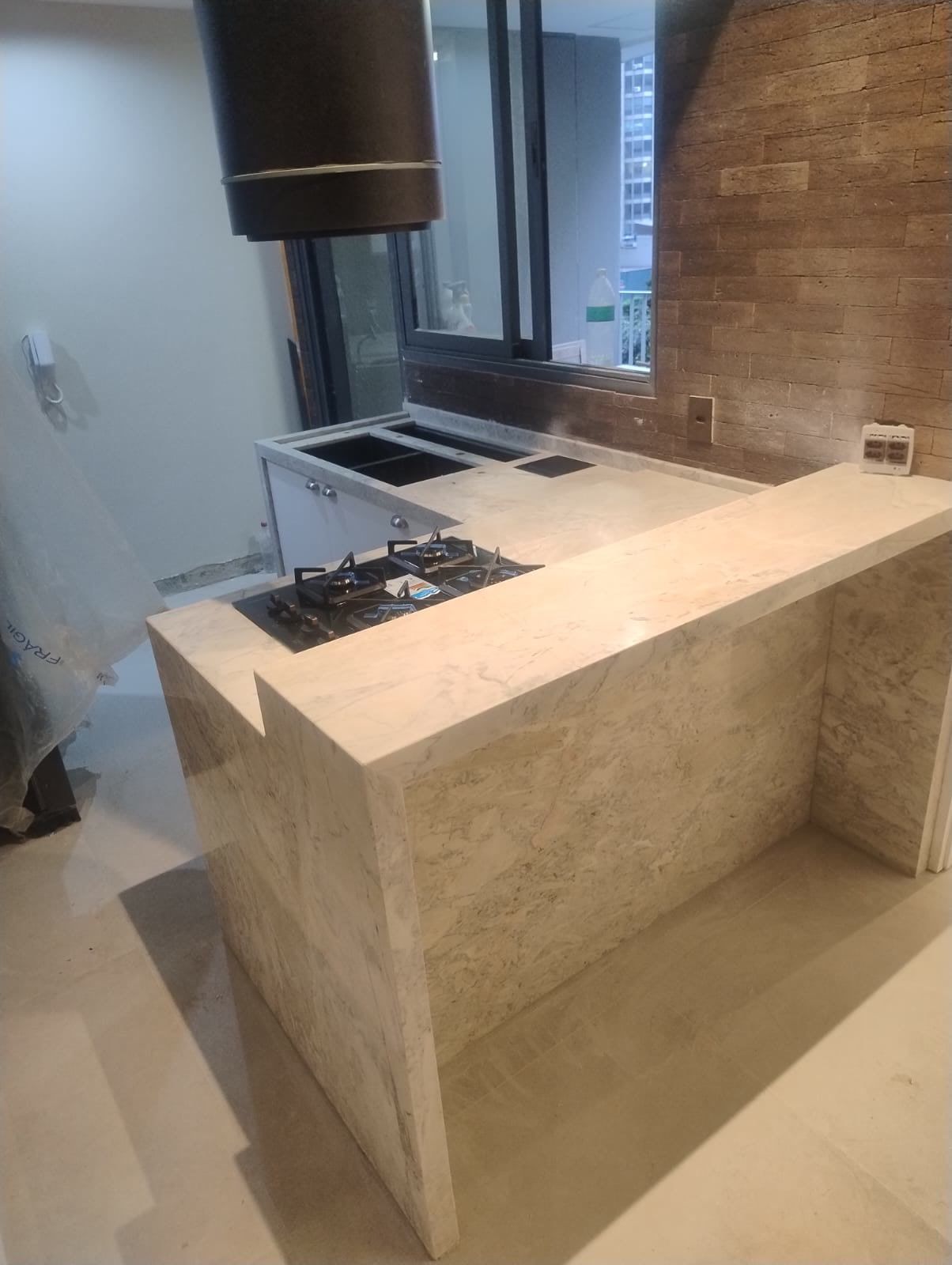Península de pedra clara com cascata, cooktop e banquetas